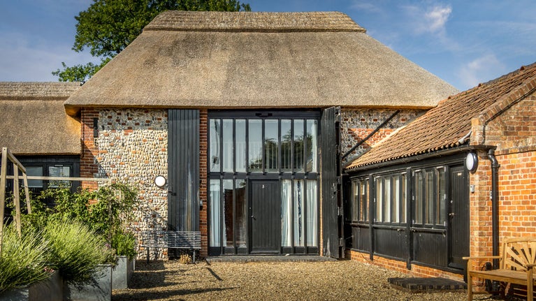 The front exterior of 3 Horsey Barns, with two-storey glazed windows and thatched roof, Norfolk